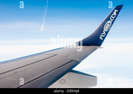 Colpo da aereo finestra e mostra il logo flyniki.com sull'ala di aeroplano, con blu cielo nuvoloso e aeroplani contrails in retro Foto Stock