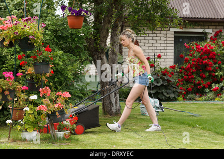 Donna mows il giardino con tosaerba elettrico Foto Stock