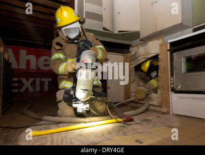Alta scuola fire academy studenti entrano ostacolo-riempito casa cercando intrappolato 'degli occupanti durante l'esercizio Foto Stock
