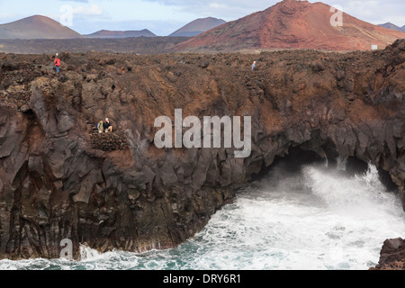 I turisti in una visualizzazione di balcone con una grande onda schiantarsi dentro una grotta marina in scogliere di Los Hervideros Lanzarote isole Canarie Foto Stock