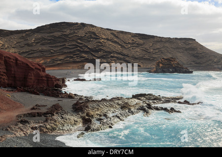 Onde infrangersi sul nero spiaggia di ghiaia circondata da rocce colorate vicino a El Golfo, Lanzarote, Isole Canarie, Spagna Foto Stock