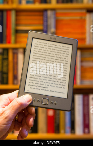 La tenuta di un Amazon Kindle nella parte anteriore di uno scaffale Foto Stock