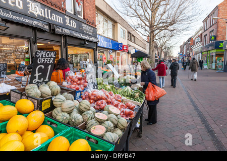 Persona per negozi di frutta e verdura presso un fruttivendolo tra gli altri negozi locali su una strada pedonale, Beeston, Nottinghamshire, England, Regno Unito Foto Stock