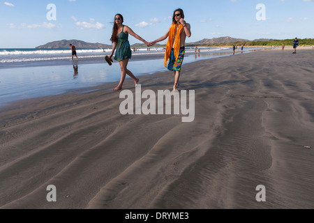 Un giovane Costa Rican giovane tenendo le mani a piedi verso il basso sulla spiaggia a Playa Tamarindo, Guanacaste in Costa Rica Foto Stock
