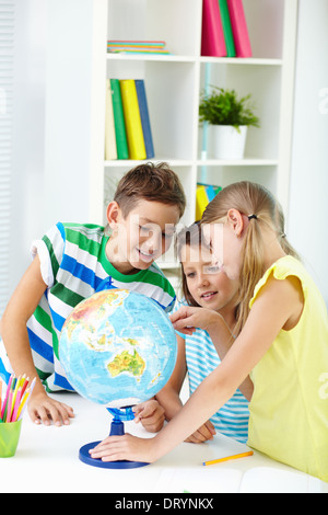 Ritratto di curiosi i compagni di scuola al lavoro studiando globe in aula Foto Stock