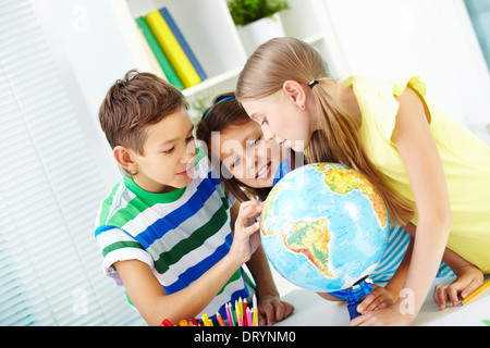 Ritratto di felice i compagni di scuola al lavoro studiando globe in aula Foto Stock