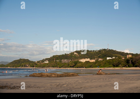 Una vista lungo la spiaggia e la città con le colline alle spalle di Playa Tamarindo, Guanacaste in Costa Rica Foto Stock