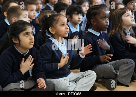 I bambini di una scuola insieme cantando e battendo le mani ed esecuzione di azioni Foto Stock