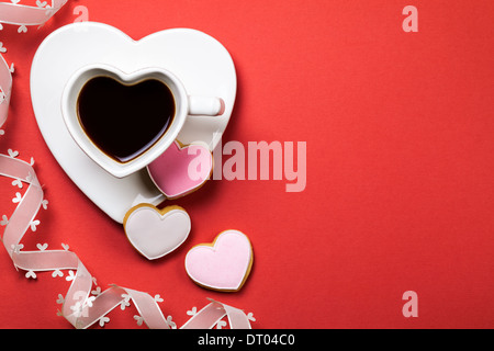 Caffè con biscotti a forma di cuore su sfondo rosso. Composizione per il giorno di San Valentino. Vista dall'alto. Spazio di copia Foto Stock