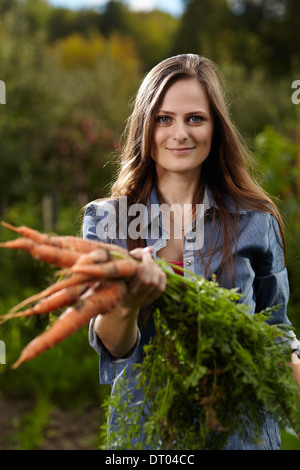 Giovane donna giardiniere tenendo un covone di carote nel suo giardino, il fuoco selettivo Foto Stock