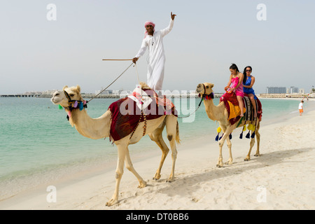 I turisti facendo un giro in cammello sulla spiaggia di Marina District di New Dubai negli Emirati Arabi Uniti Foto Stock