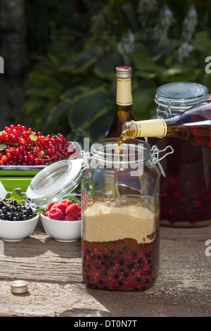 Il Brandy versando da una bottiglia in un grande vaso di inscatolamento con purea di frutta e zucchero di canna Foto Stock