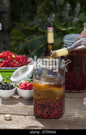 Il Brandy versando da una bottiglia in un grande vaso di inscatolamento con purea di frutta e zucchero di canna Foto Stock