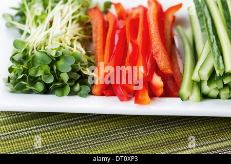 Ingrandimento orizzontale della foto appena affettato peperoni rossi, posto nella piastra bianca, insieme con fette di cetrioli e rafano daikon Foto Stock