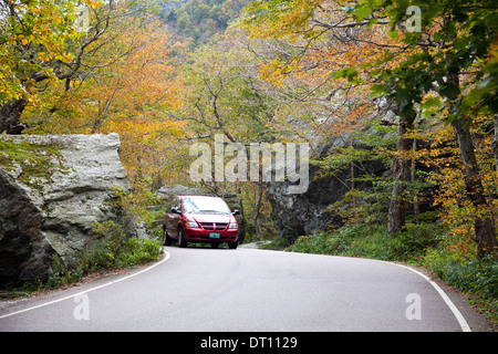 Auto rossa si avvicina a sommità di Smugglers' Notch (VT 108) attraverso il grazioso alberi sul lato ovest della strada in Vermont montagne verdi. Foto Stock