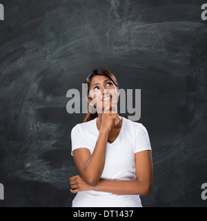 Felice donna indiana in piedi di fronte a una lavagna scuro. Chalk board è vuoto in attesa di un messaggio. Foto Stock