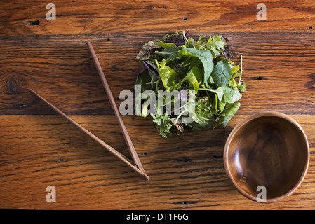 Un piccolo giro in legno lucido di ciotola e una frizione di organico miscelato foglie di insalata con le bacchette di legno Foto Stock