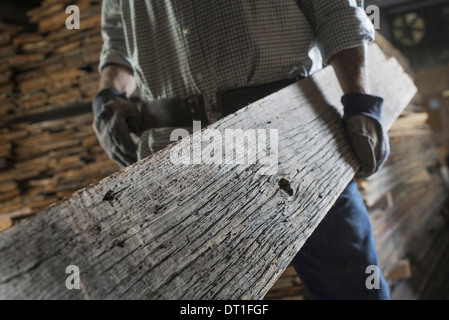 Un cumulo di materiale riciclato rigenerato listoni di legno di legno ambiente un uomo che porta una grande tavola di maturare in legno stagionato Foto Stock