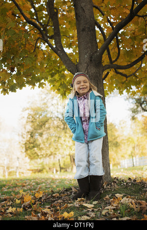 Una giovane ragazza in piedi sotto un albero in una fattoria di fogliame di autunno Foto Stock