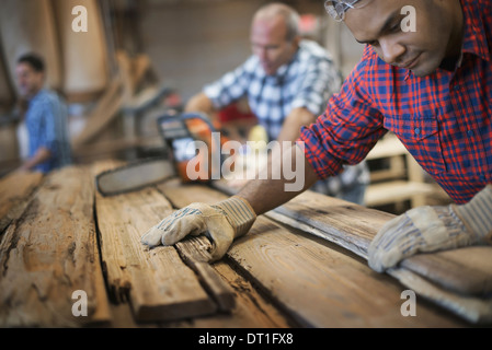 Un legname rigenerati workshop di un gruppo di persone che lavorano un uomo di misura e controllo di tavole di legno per il riutilizzo e il riciclo Foto Stock