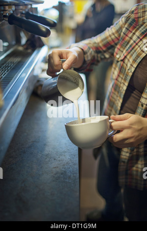 Una persona barista il caffè e la colata della schiuma di latte da una brocca in una coppa per un cappuccino Coffee shop Foto Stock