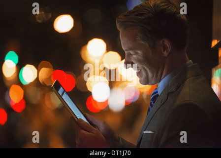 Un uomo in una città di notte guardando un computer tablet Foto Stock