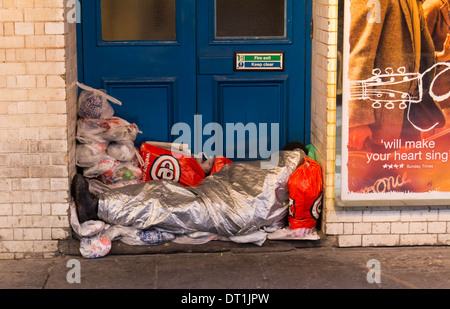 LONDON, Regno Unito - 1 FEB 2014: una persona senza dimora avvolto in un foglio di copertura in una porta di un edificio con sacchetti di plastica tutti aroun Foto Stock