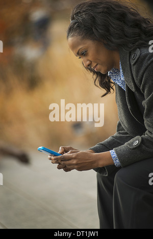 Una donna in un rivestimento di controllo e texting mantenendo in contatto utilizzando un telefono cellulare Foto Stock