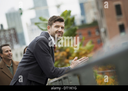 Un uomo in un cappotto appoggiato su di una ringhiera prendendo il tempo fuori il paesaggio della città di edifici Foto Stock