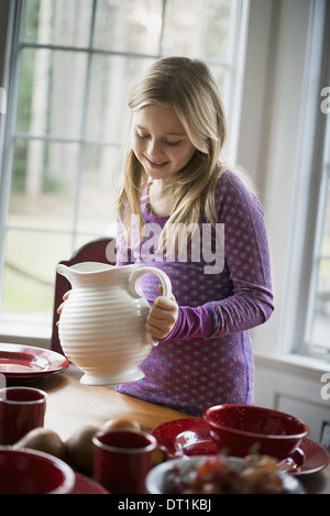 I bambini in una casa famiglia una ragazza con un bianco Caraffa in ceramica tavolo apparecchiato con stoviglie Foto Stock