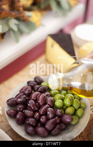 Fresche verdure organiche verde e olive nere drizzling di olio di oliva da un flacone preparato farm stand alimenti per un partito Foto Stock
