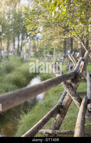 Un rurale scena vista su una staccionata di pali di legno di un piccolo ruscello di alberi con vivaci foglie verde Foto Stock