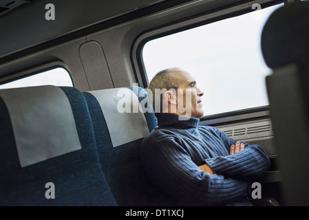 Un uomo maturo seduto in un posto vicino al finestrino su un viaggio in treno guardando fuori nella distanza Foto Stock