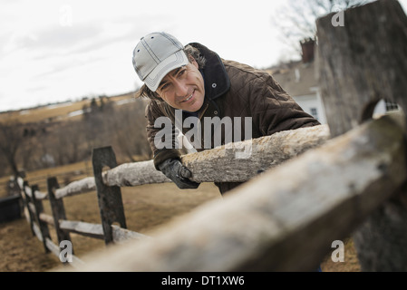 Uomo appoggiato a un post e cancellata in una fattoria in inverno Foto Stock