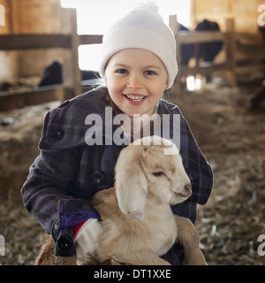 Un bambino nel capannone animale holding e accarezzare un bambino di capra Foto Stock