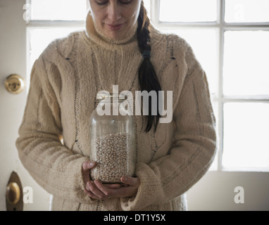 Una donna in un cavo a maglia maglione tenendo un vasetto di vetro di fagioli bianchi Foto Stock