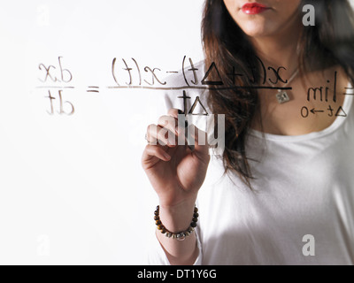 Una giovane donna a scrivere una equazione matematica con pennarello nero su un chiaro vedere-attraverso la superficie Foto Stock
