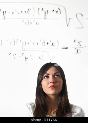 Una giovane donna a scrivere una equazione matematica con pennarello nero su un chiaro vedere-attraverso la superficie e in piedi indietro a prenderla in considerazione Foto Stock