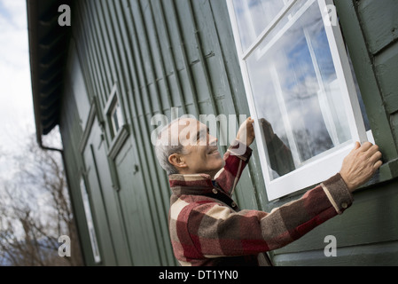 Un agriturismo biologico in manutenzione invernale di un uomo con una finestra temporale pannello contro il telaio della finestra Foto Stock