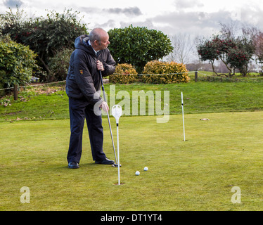 Senior uomo putts con 'soon ad essere vietate' lungo putt sul putting green a Sunbury Golf Center Foto Stock