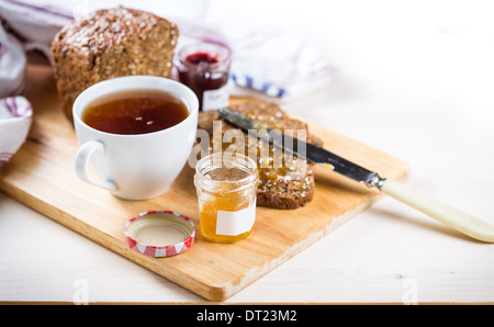 Pezzi di pane, una tazza di tè e un vasetto di marmellata di arancio Foto Stock