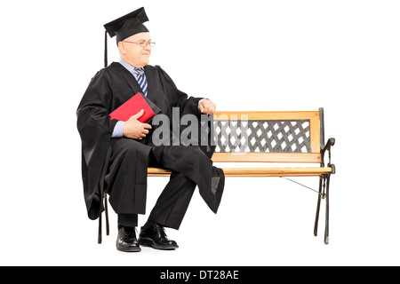 Uomo maturo in abito di graduazione seduto sulla panca di legno e libri di contenimento Foto Stock