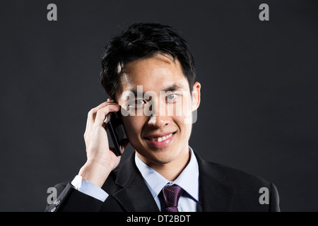 Ritratto di un elegante Asian business man utilizzando un telefono intelligente. Sfondo grigio scuro Foto Stock
