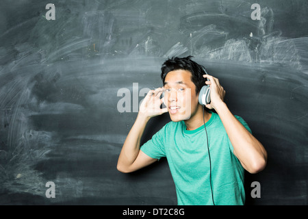 Bel uomo asiatico che indossa gli auricolari di cantare e ballare con la musica. In piedi di fronte a una lavagna. Foto Stock