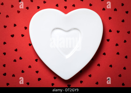 Forma di cuore piastra bianca su carta rossa sullo sfondo. Vista superiore Foto Stock