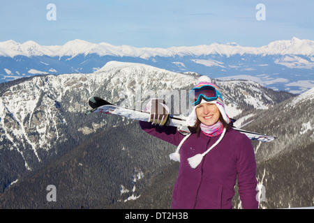 Sorridente bella ragazza il trasporto di sci con pittoreschi inverno sfondo montagnoso Foto Stock