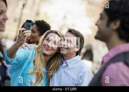 La gente all'aperto nella città in primavera una donna con il suo telefono cellulare per scattare una fotografia di un gruppo di amici che le donne e gli uomini