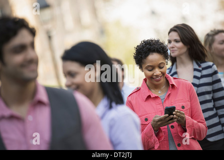 La gente all'aperto nella città in primavera una donna in piedi tra un gruppo controllo il suo telefono cellulare Foto Stock