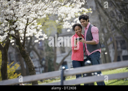 New York City Park di un uomo e di una donna a fianco a fianco di prendere una fotografia con una mano il telefono cellulare Foto Stock