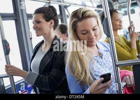 La città di New York uomini e donne su un autobus del trasporto pubblico mantenendo in contatto una giovane donna di controllo o utilizzando il suo telefono cellulare Foto Stock